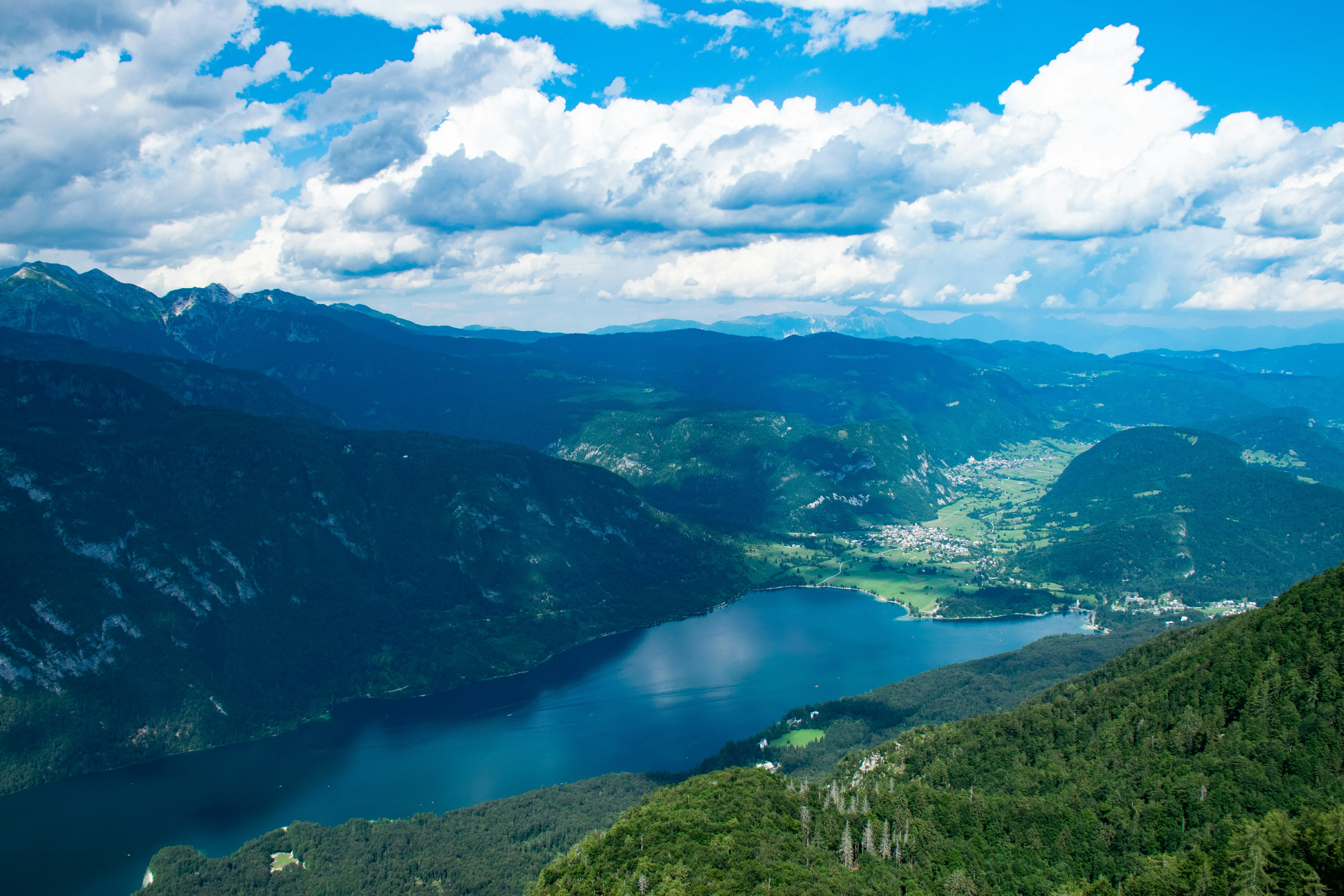 Green mountains around Lake Bohinj under white clouds and blue sky